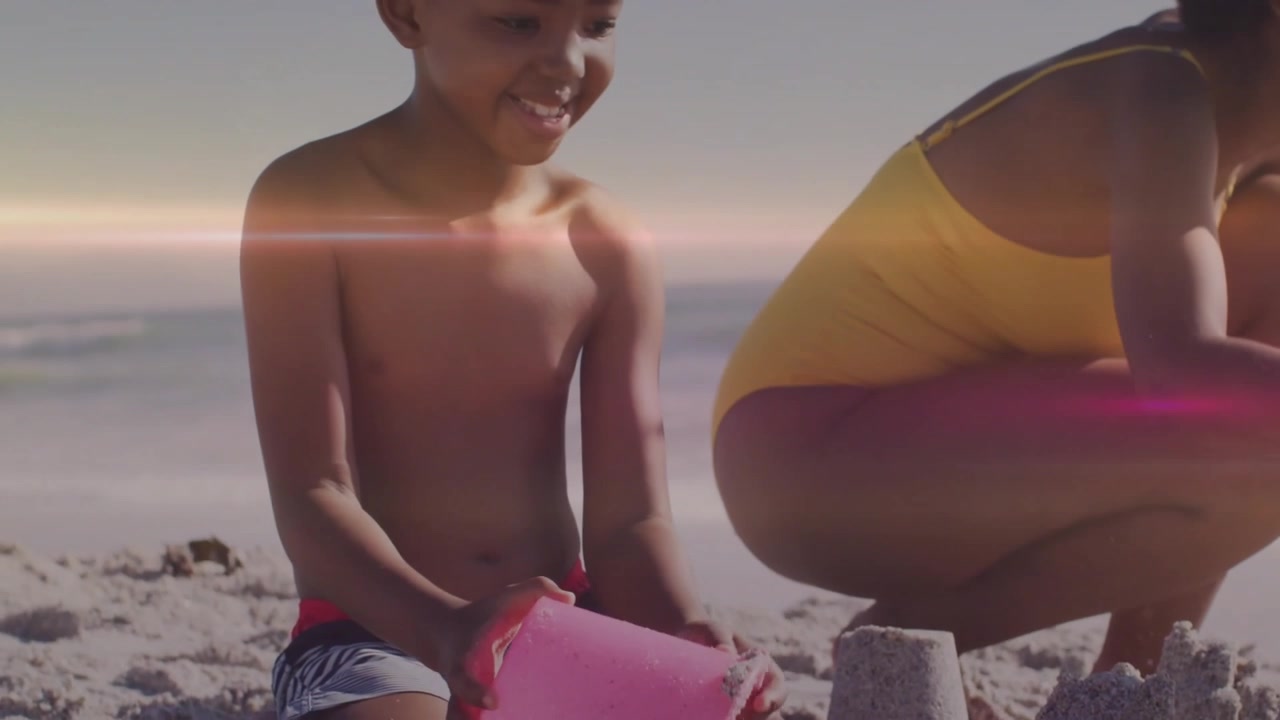 Un bambino usa una paletta e inizia a scavare nel secchiello rosa mentre la madre modella torri per i turisti.