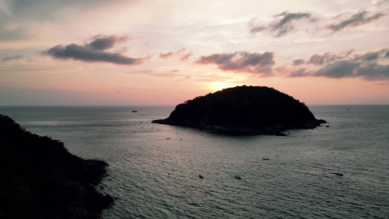 Stunning sunset view over Yanui Beach in Phuket, Thailand, with small boats scattered across calm sea and silhouetted island in golden light