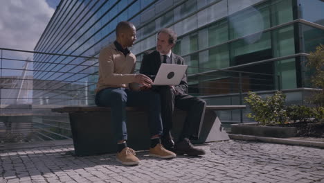 Multicultural-professional-managers-discussing-projeсt-with-laptop-outdoors