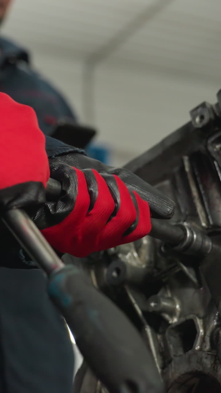 primer plano de un ingeniero con un pendiente magnético usando una llave inglesa para aflojar una nuez en un motor, con guantes rojos, mientras su colega observa el proceso en el taller