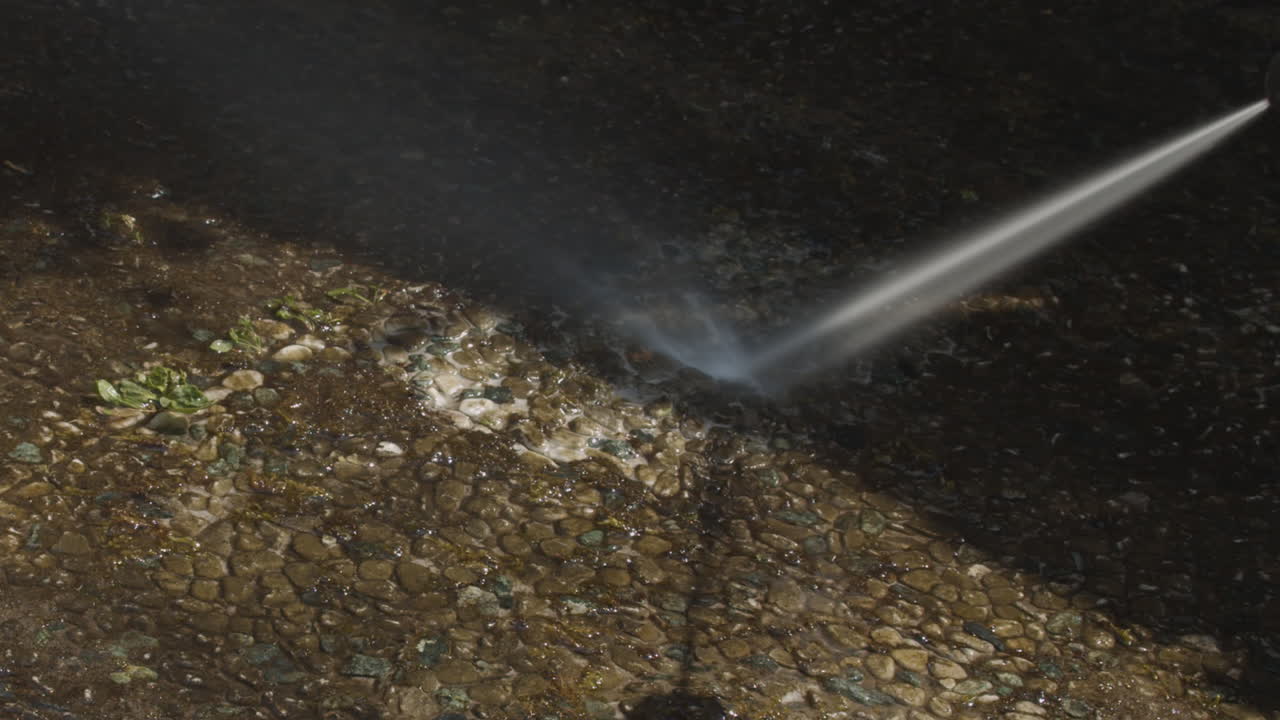 Potente getto d'acqua da idropulitrice spruzzato su erbacce e muschio su una piastrella da giardino sporca - zoom indietro dinamico