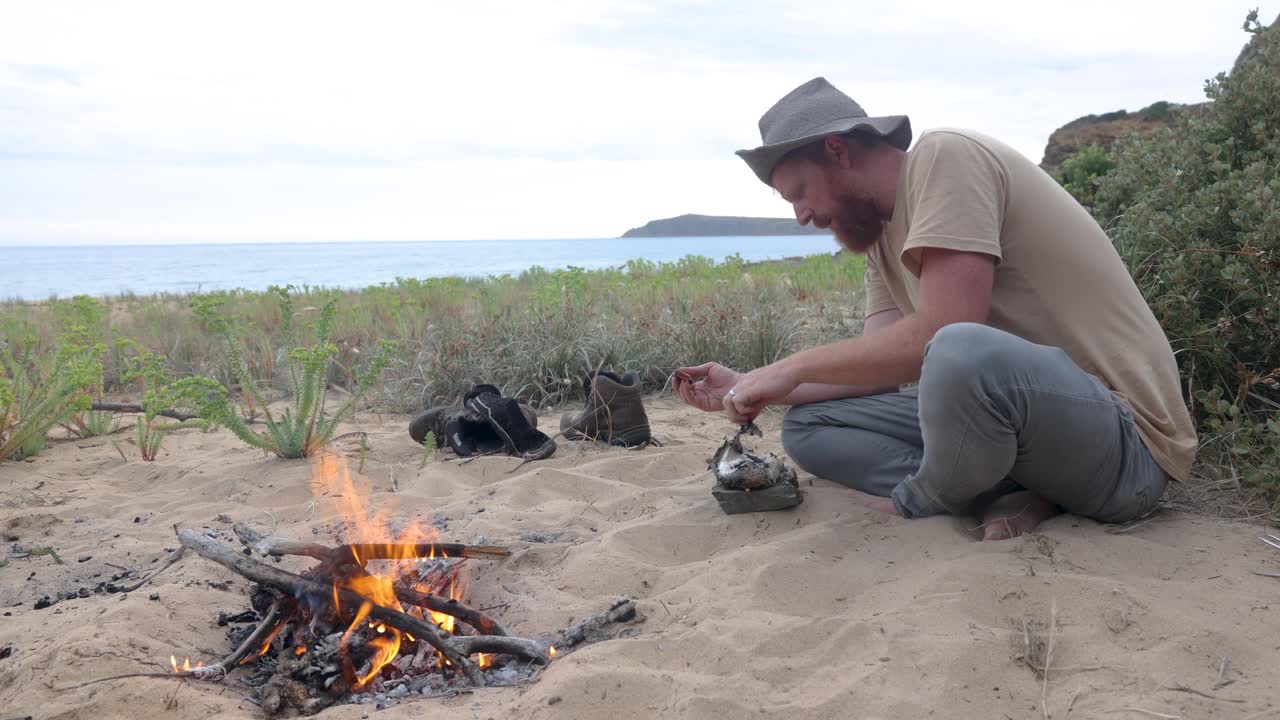 un hombre de supervivencia costera comiendo pescado en una fogata junto al océano