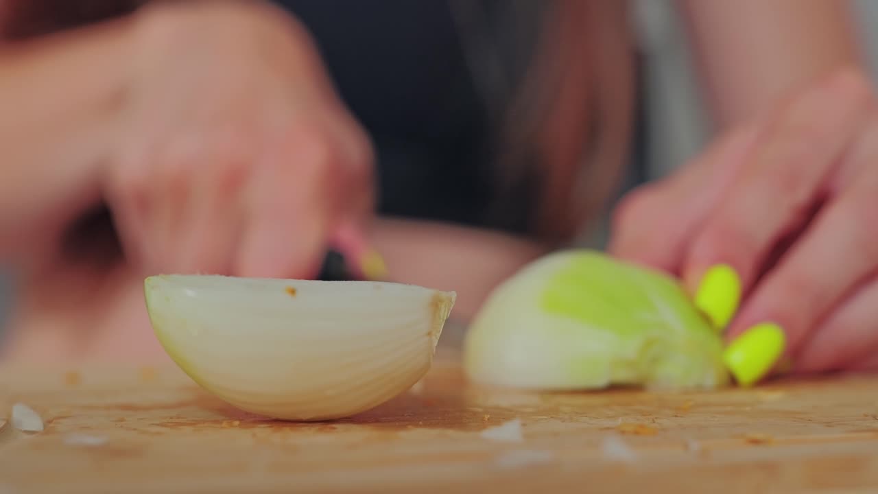 Static close up of onion half in focus while woman slices other piece blurred