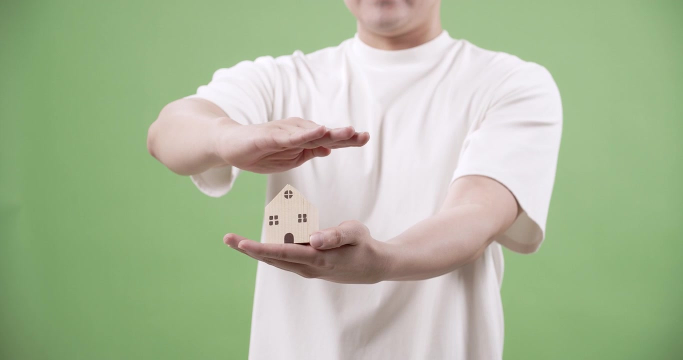 Un uomo dimostra l'importanza della protezione domestica proteggendo una casa in miniatura che simboleggia sicurezza e incolumità per i proprietari di casa.