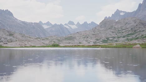 la lluvia cae ligeramente en el pacífico lago alpino con picos de montaña detrás