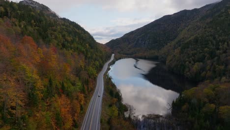 a car is passing by a lake surrounded with fall colors in upstate new york