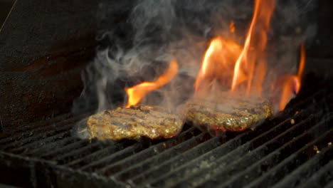 burger patty grilled over flame, fire and smoke flare up around hamburger meat, slide slow motion