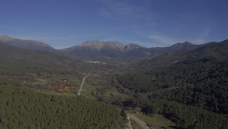 reverse flight in a valley with lush pine forests and in the background large mountains with a road with cars in circulation that leads to a mountain pass on an autumn day with in avila-spain