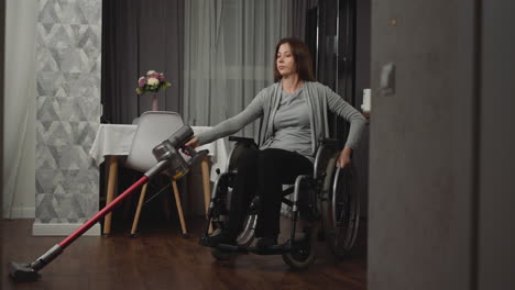 young housewife vacuums floor in room moving in wheelchair