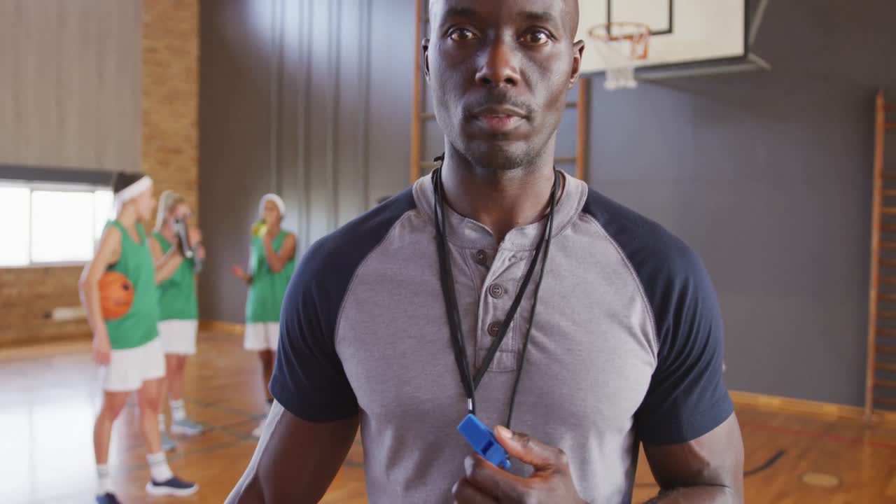 Portrait of african american male coach with diverse female basketball team in background