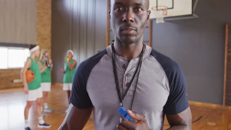 Portrait-of-african-american-male-coach-with-diverse-female-basketball-team-in-background