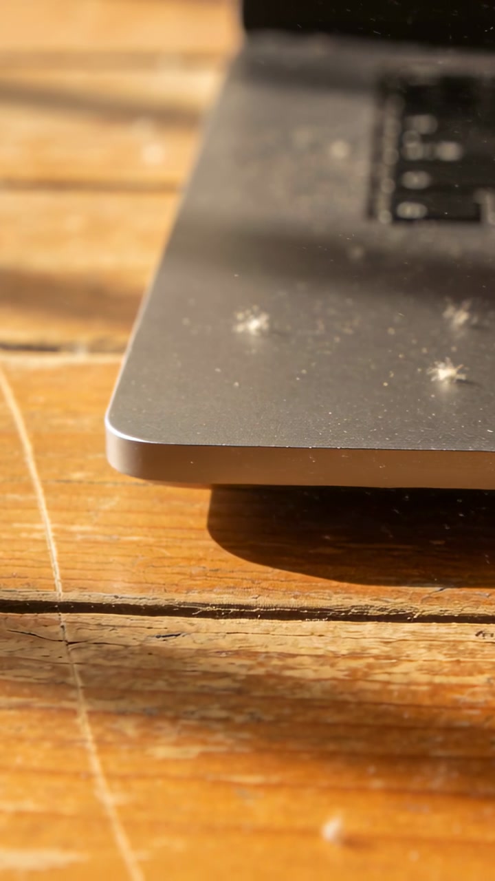 Vertical video: Sunlight from left causing dust motes drifting over silver laptop on wood table