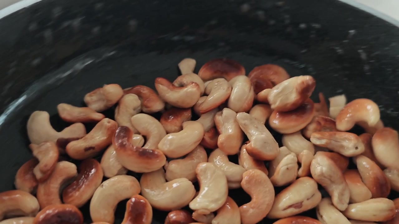 Ultra-kinematisk sakte film av risting av cashewnøtter i svart panne med olivenoljesprut, makro matkunst nærbilde, sprø gyllen transformasjon, gourmetkjøkken ASMR visuell fest. 4K HDR viralt arkivmateriale NÅ.