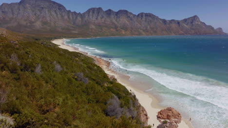 south africa aerial drone garden route koeel bay dappat se gat cinematic windy grass surf waves crashing kogel bay beach cape town coastline aqua deep blue water gordon's bay forward pan up movement