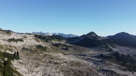 luchtfoto van mount brew met rotsachtig landschap en pijnbomen die pannen om zonreflecterend meer en wazig bergterrein in canada bc 4k te onthullen