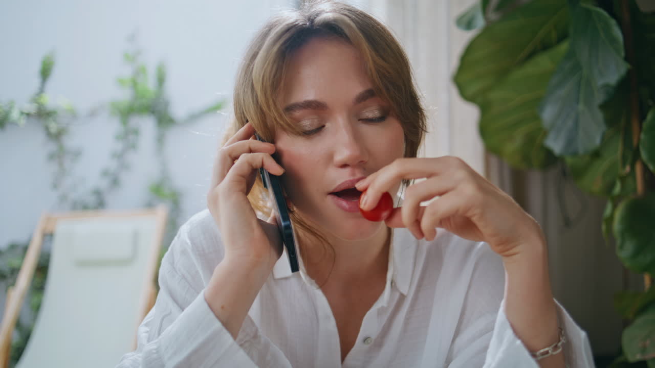 Eating woman speaking smartphone at cozy home interior closeup. Smiling lady