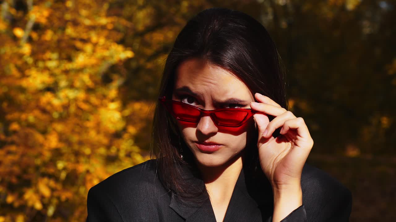 A Stylish Individual in Dark Attire and Red Sunglasses Poses Amidst Autumn Foliage, Highlighting a Fusion of Fashion and Nature