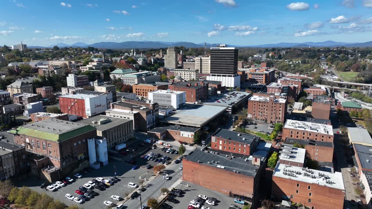 Aerial descend shot of Lynchburg Town in Virginia during sunny day. Downtown with historic buildings and parking cars on parking lot. Wide shot. Sunny day with blue sky in October.