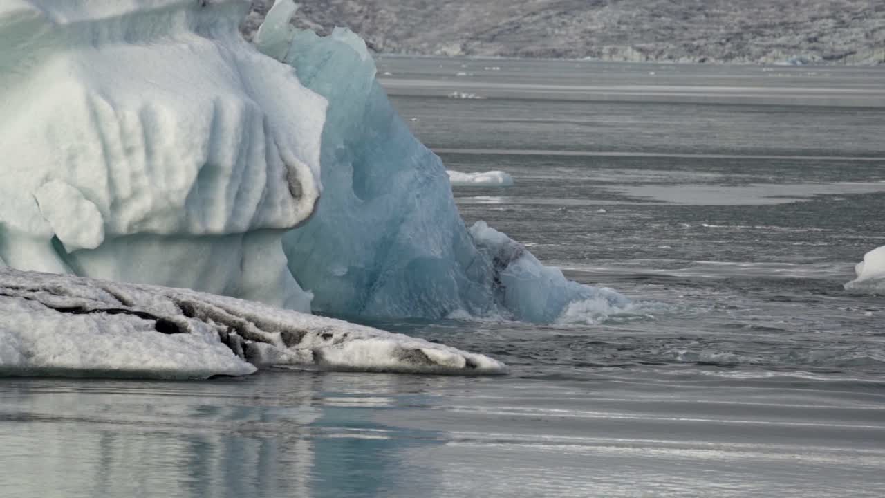 A vibrant turquoise-blue iceberg, a colossal fragment of ancient ice, majestically drifts across the serene, grey waters of Iceland's iconic Jökulsárlón Glacial Lagoon