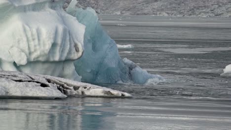 a vibrant turquoise-blue iceberg, a colossal fragment of ancient ice, majestically drifts across the serene, grey waters of iceland's iconic jökulsárlón glacial lagoon