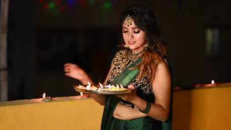 beautiful young woman lighting diya - oil lamp in traditional clothing on the occasion of diwali.