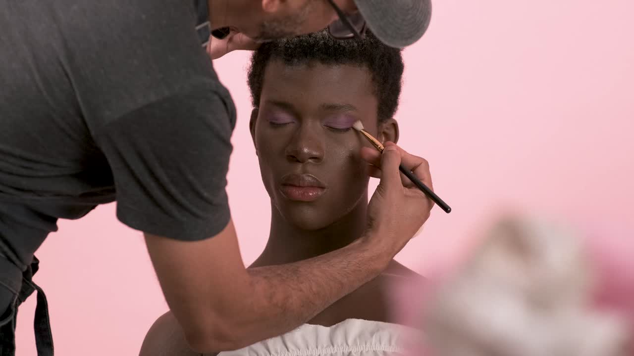 Crop visagiste doing professional makeup on transgender person