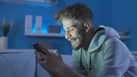 Happy-and-cheerful-young-man-using-phone-at-home.