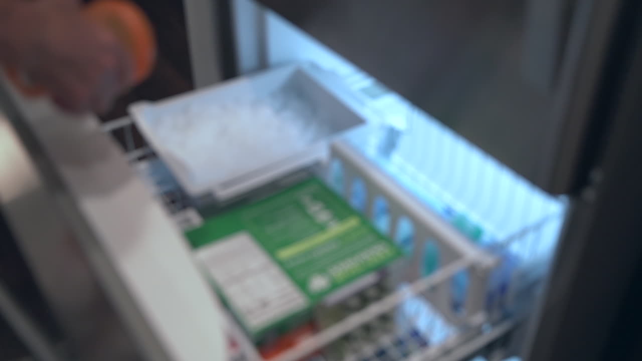 Ripresa al rallentatore, fuori fuoco, di un uomo che allunga la mano nel congelatore per riempire il suo shaker per integratori con ghiaccio fresco.