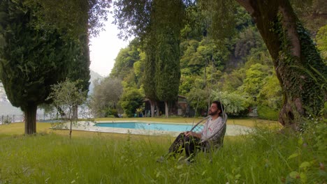back view of man sitting alone facing empty pool in lake como, italy (lago di como, italia), on a cloudy serene day