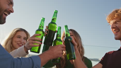 joyful friends clinking beers relaxing together on rooftop party close up.