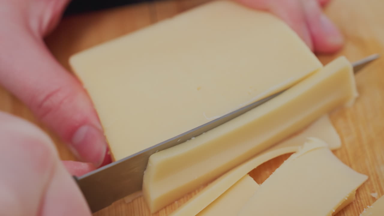 close up of person slicing butter block with sharp knife on wooden kitchen board, capturing detailed texture of butter and precision of cutting technique in food preparation process