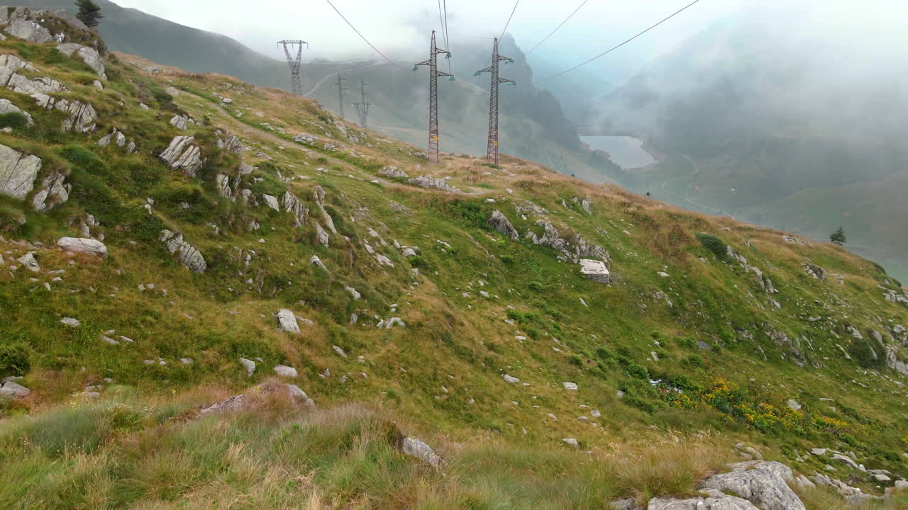 volando sobre las rocas de los campos de montaña cerca de los cables de alta tensión en passo san marco, norte de italia - toma aérea de drones
