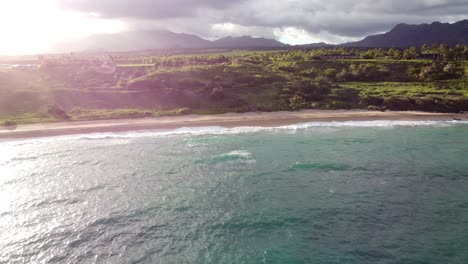 aerial view over clear, transparent ocean water foaming at the shore, washing the golden sand of the beach, green mountains