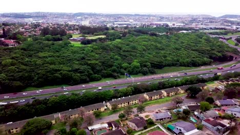 Imágenes-Aéreas-De-Un-Dron-Volando-Sobre-Casas-Residenciales-Con-Vistas-A-Una-Carretera-Muy-Transitada-Con-Tráfico-En-Movimiento-En-Un-Suburbio-De-Yellow-Wood-Park-En-Durban