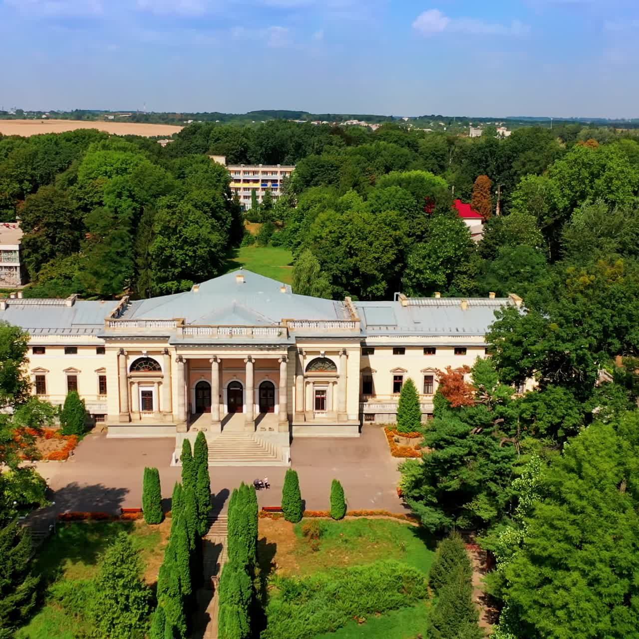Beautiful palace with columns surrounded by the green park. Urban area with low cottages at backdrop. Sunny day footage from top