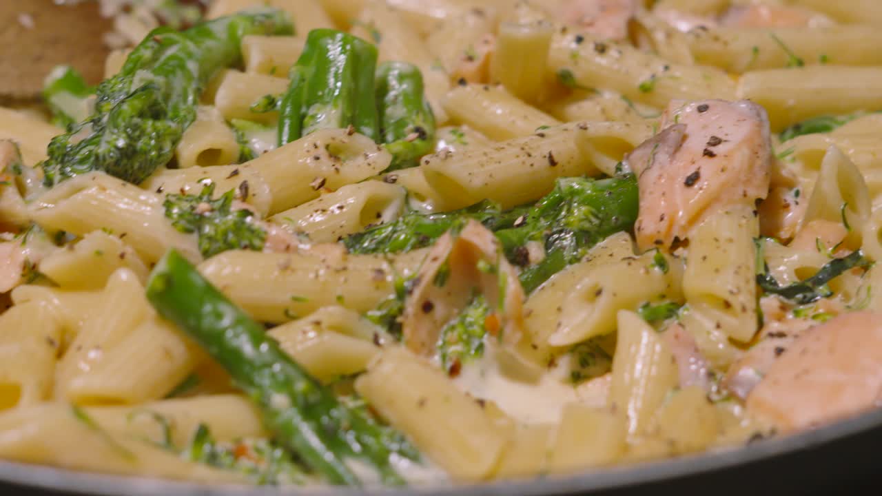 Spin and Pan View Over Delicious Salmon and Broccoli Penne Italian Pasta on Gas Stove with Cracked Black Pepper. Cooking Kitchen Seafood Healthy Eating Footage 4K.