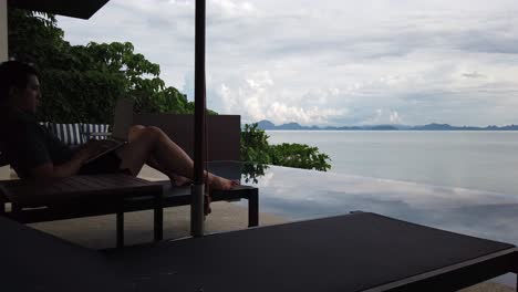 asian man working on the laptop by the pool - back view