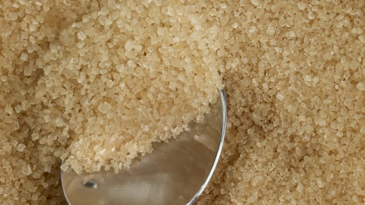Close-up video of raw brown sugar being scooped by a spoon, highlighting texture and granularity under soft lighting