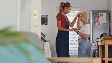 Happy-diverse-female-couple-cooking-vegetables-and-dancing-in-kitchen