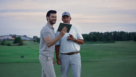 wealthy men video call tablet device on golf course. friends talk online outside