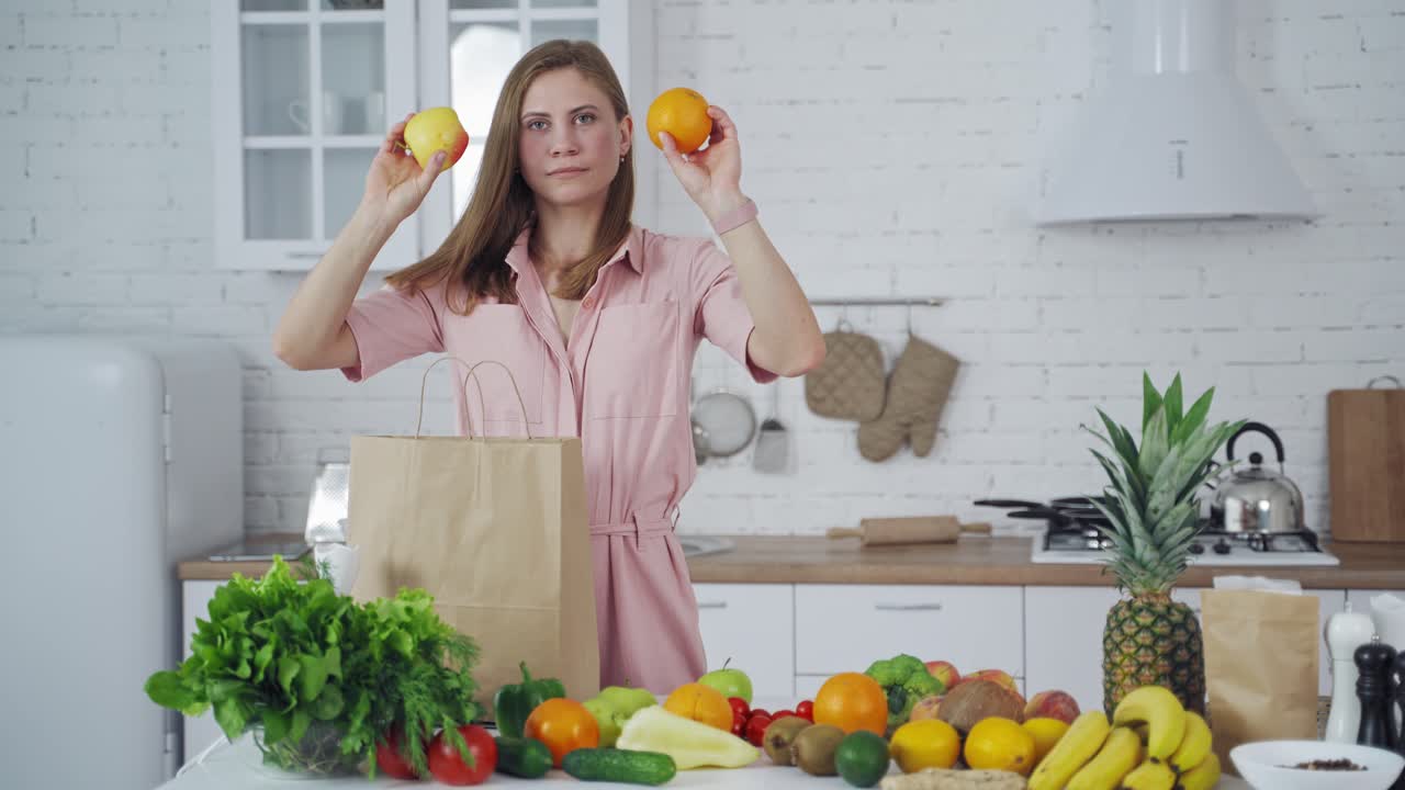 Lovely young woman takes out of a bag organic fruit in the light kitchen. Young model cares about healthy diet. Healthy food on the table.