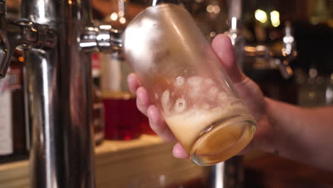 bartender pulls draft amber beer into frosted pint glass, tracking close up hd