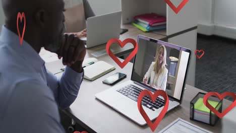 animation of red heart icons falling over african american man having video call on laptop at office