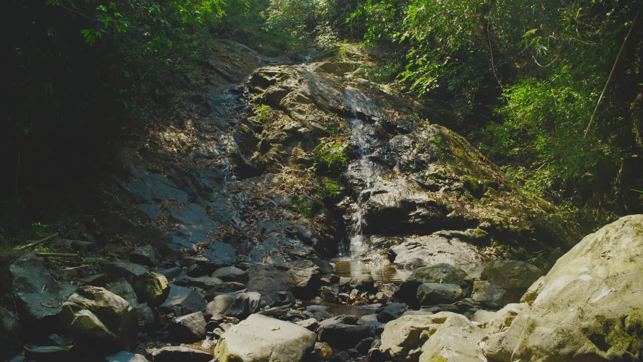 Et fredfyldt vandfald kaskader ned ad stenet terræn omgivet af frodigt grønt i Khao Sok Nationalpark