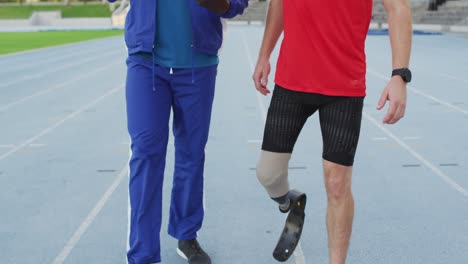 diverse male coach and disabled athlete with running blade talking during training session