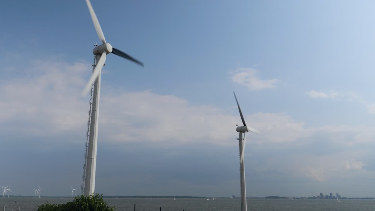 두 개의 빠르게 회전하는 풍력 터빈이 바다 풍경과 구름이 가득한 하늘을 향해