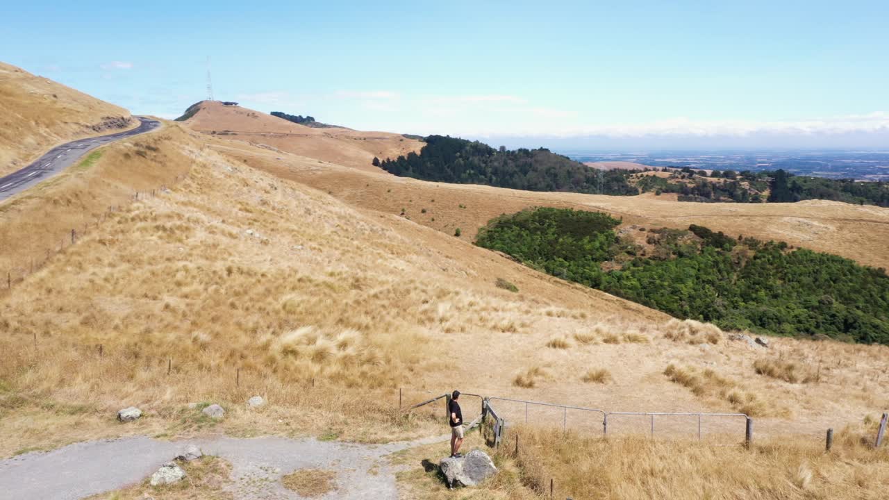 Point of interest aerial shot of man standing on rock on a hill looking at view
