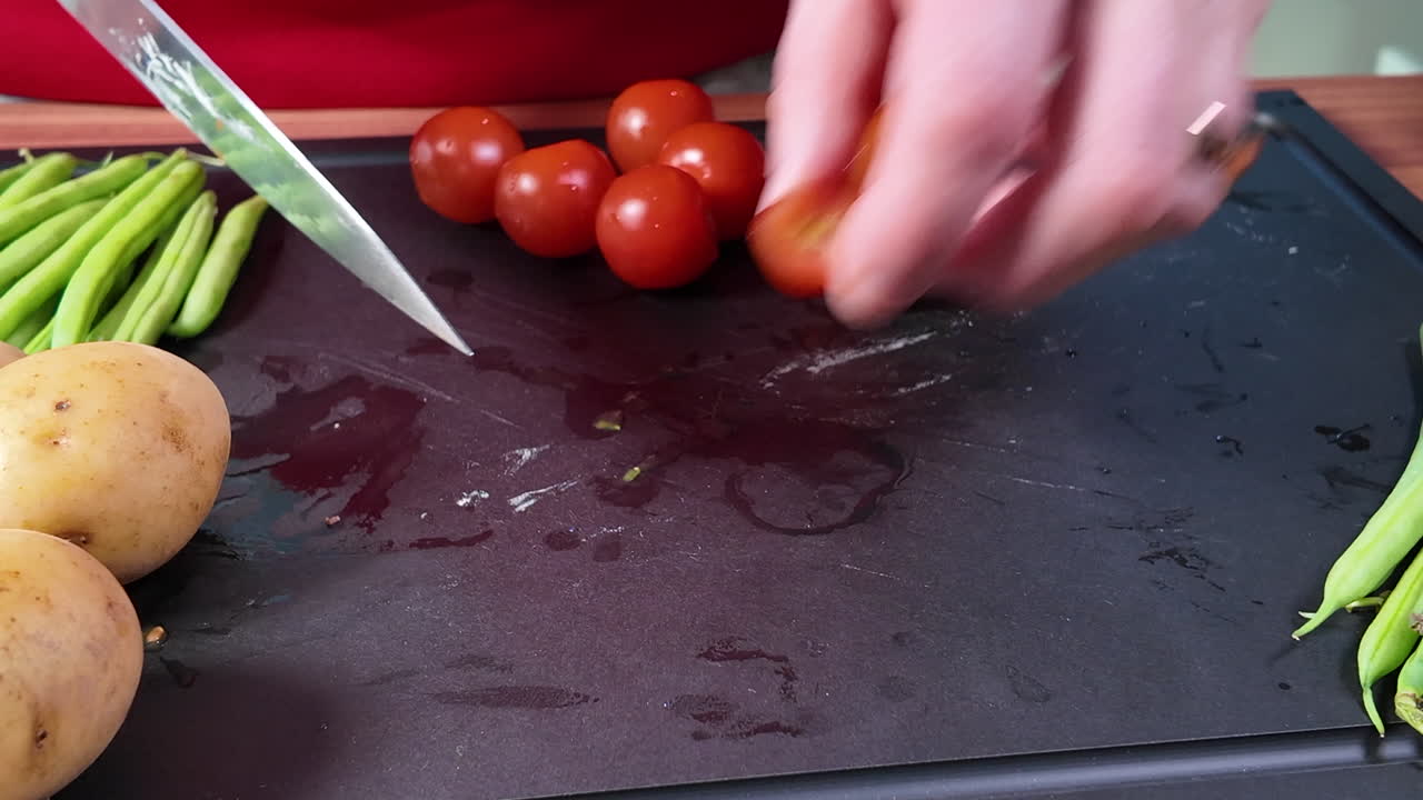 Close-up shot of hands slicing fresh cherry tomatoes into pieces on a cutting board using a sharp kitchen knife