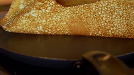 flipping a pancake with wooden spatula in a frying pan. close up, slow motion.
