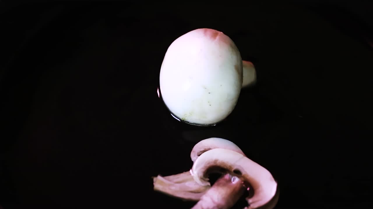 Mushroom slices splashed by other pieces on a liquid surface with water on dark background in slow motion
